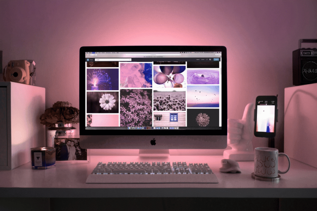 Professional web design workspace featuring iMac displaying colorful website layouts with ambient pink lighting - Develoroo creative environment